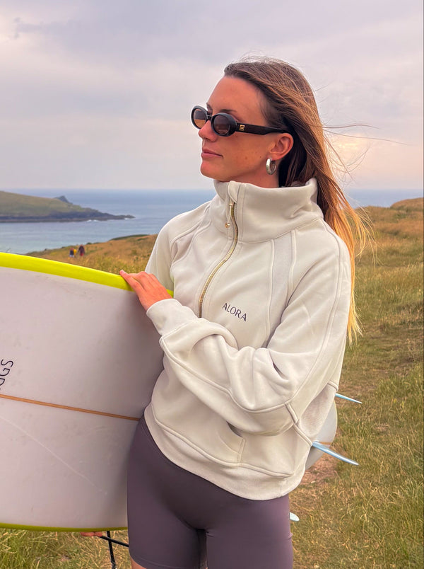 Woman holding a surfboard on a grassy hill with a scenic background